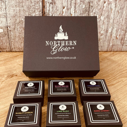 Set of Northern Glow wax melts boxes on a wooden surface with a branded box in the background.