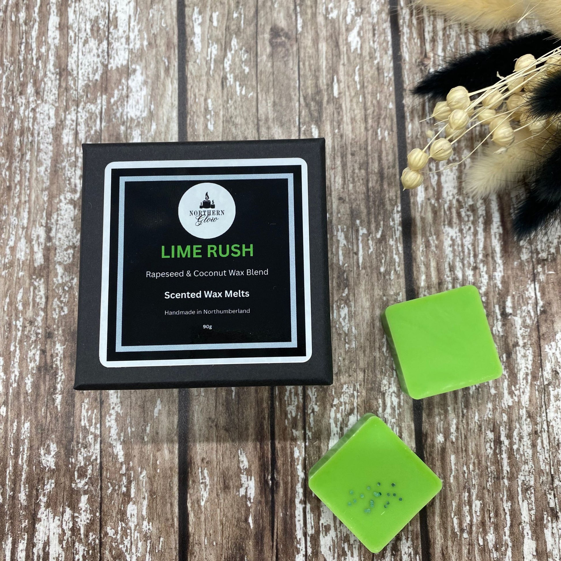 Lime Rush wax melt is in a small black box with the writing Lime Rush in green writing. The box is placed on a wood backgrounfd.