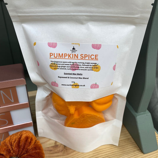 A white bag with orange colour pumplin shaped wax melts, also a jumper shaped wax melt. The label is white and orange