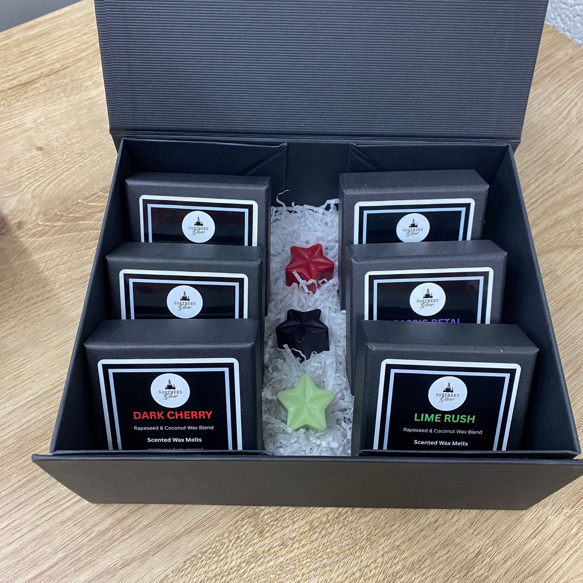 Set of scented wax melts in black boxes with labels on a wooden surface