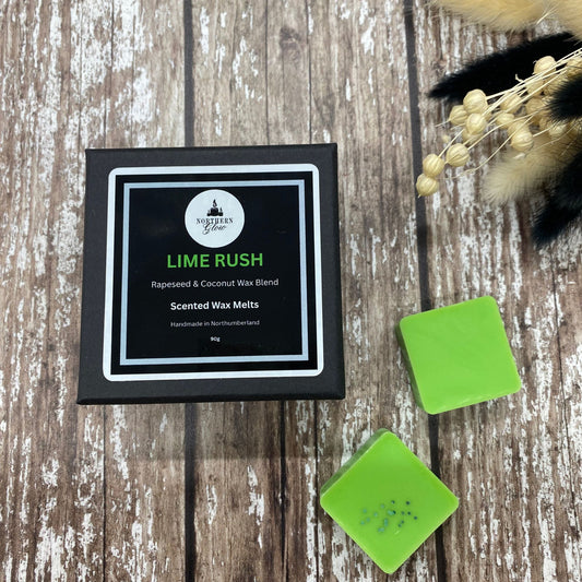 Lime Rush wax melt is in a small black box with the writing Lime Rush in green writing. The box is placed on a wood backgrounfd.