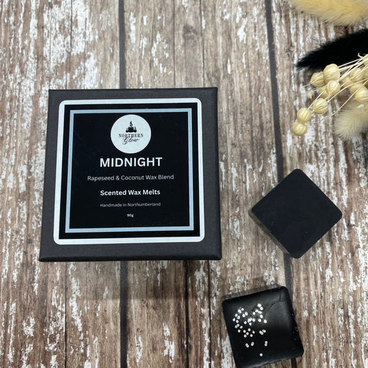 The wax melts are in a small black box with the wording Midnight in white writing. The box is placed on a wood background.