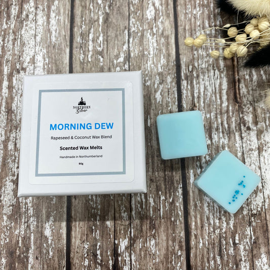 Light Blue wax melts in a square shape next to a white box on a wooden stand