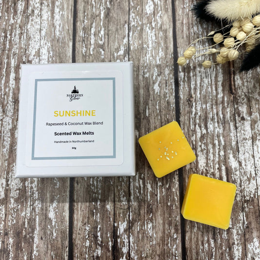 Sunshine wax melt is a yellow colour and each melt is a square shape in a white box. There are eight individual wax melts in the white box. The label is white with a silver border. The logo is at the top with 'Sunshine' in yellow writing in the centre.