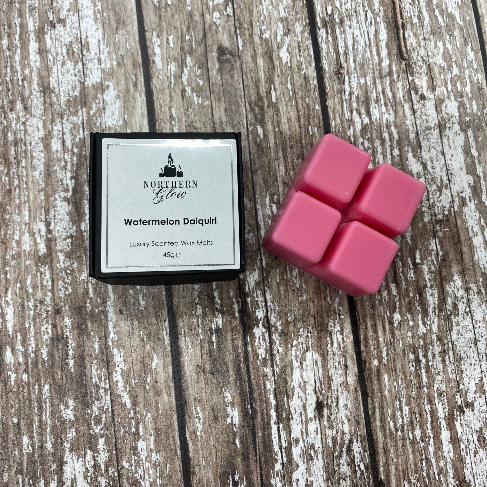 Watermelon Daiquiri Wax Melt is a pink colour and is a square shape with four breakable cubes in a plastic case. The lable is white with a silver border and black writing. The logo is at the top with 'Watermelon Daiquiri' in the centre