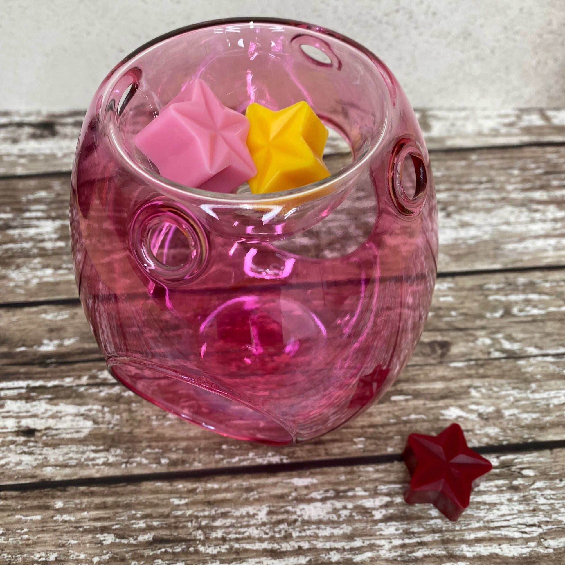 This wax melt burner is pink with three wax melts, two inside the top of the burner and one next to it.  The burner is pink glass