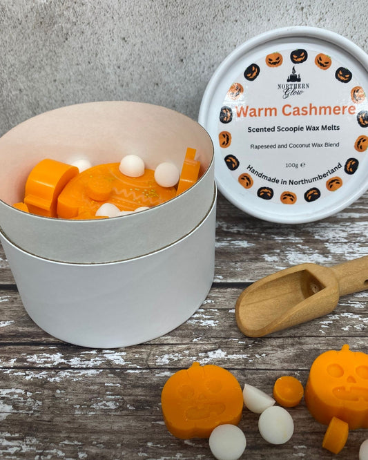 Northern Glow Warm Cashmere scented scoopie wax melts in a white round tub with Halloween-themed lid and orange and black writing.